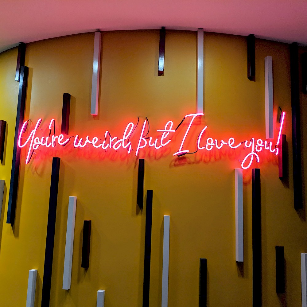 neon sign reading “You’re weird, but I love you”