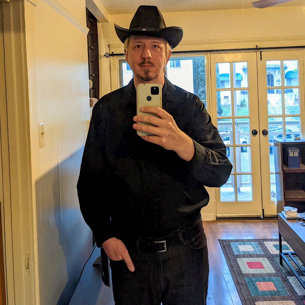 selfie wearing all black pants, shirt, and cowboy hat