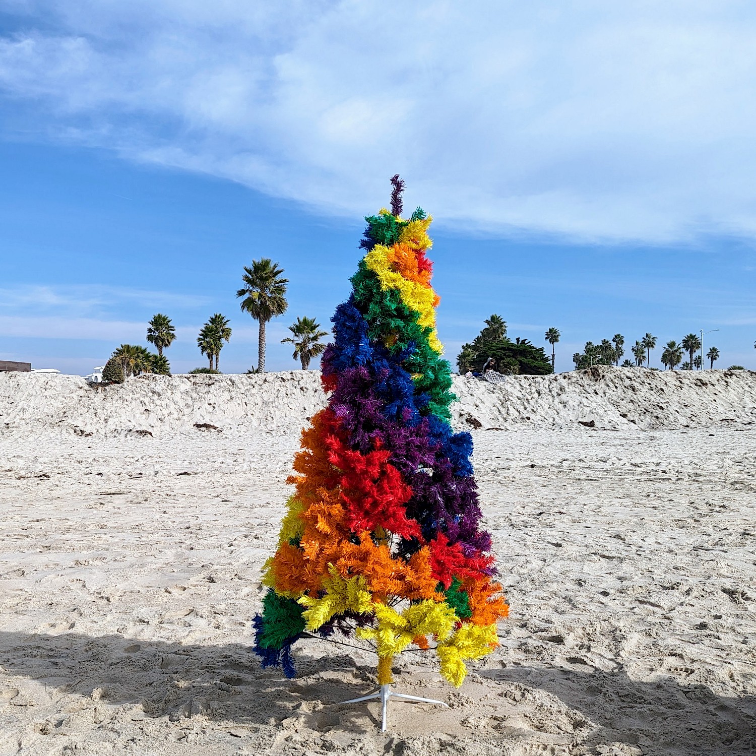 A rainbow-colored Christmas tree set up on the beach