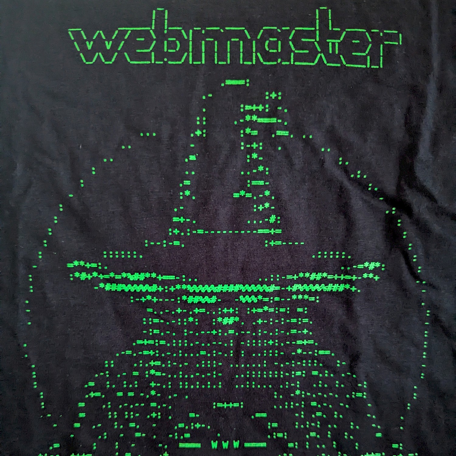 A black t-shirt with small, green ASCII characters similar to an old computer screen. Together the characters create a picture of a wizard with the word 'webmaster' above it
