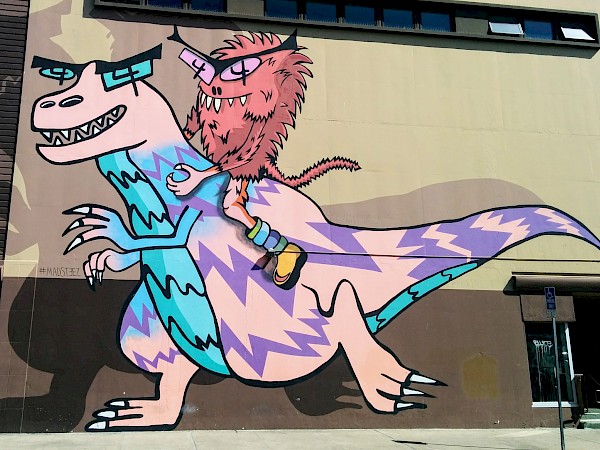 Large mural of a red, fuzzy monster riding on a T-rex that is pink with purple stripes