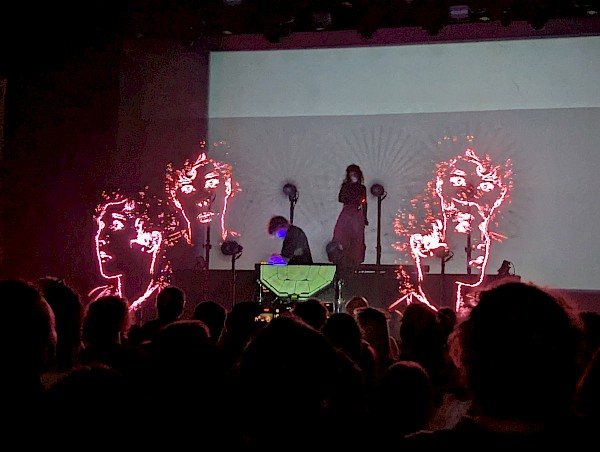 Purity Ring on stage with spinning LED lights that show video of four faces