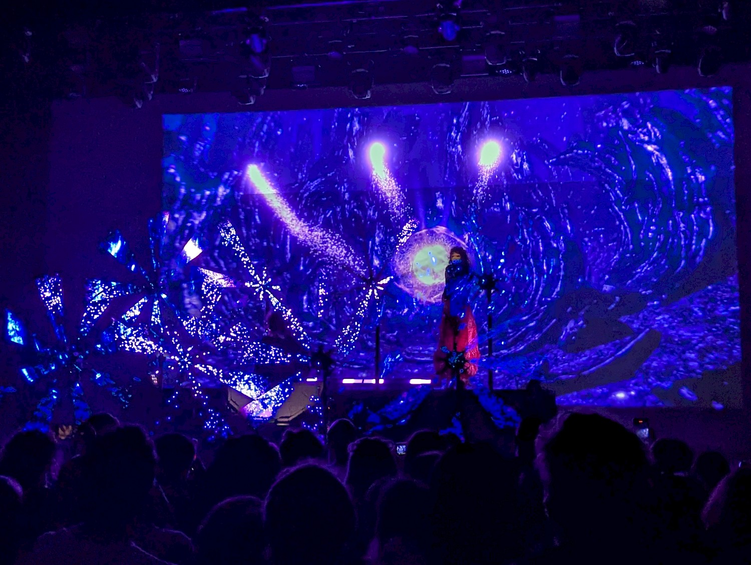 Purity Ring on stage with spinning LED lights that show video of blue sparkles flying out