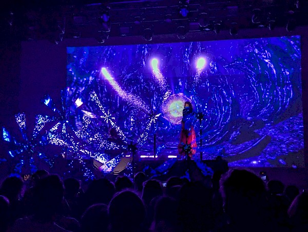 Purity Ring on stage with spinning LED lights that show video of blue sparkles flying out
