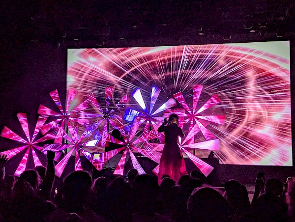 Purity Ring on stage with spinning LED lights that show video of a pink/purple-y spiral, caught mid-spin